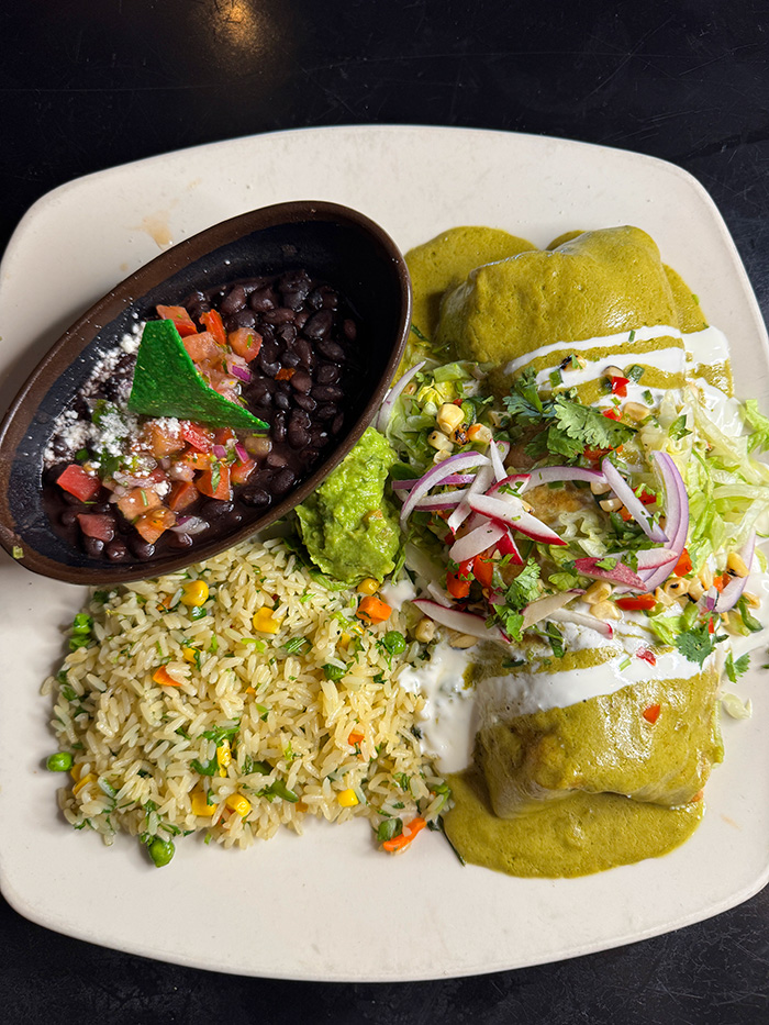 Gourmet burrito in mild tomatillo sauce and melted cheese with rice, beans, guacamole and pico